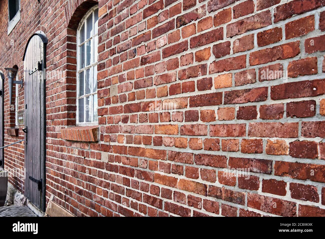 Schräge Ansicht einer roten alten verwitterten Ziegelmauer mit einem verschwommenen Fenster am Ende Stockfoto