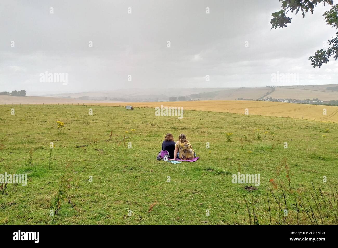 Eine Sommersturmwolke nähert sich einem Paar, das ein Picknick auf einem Hügel mit Blick auf das Wylye Valley in der Nähe von Wilton, Salisbury, macht. GROSSBRITANNIEN 2020. Stockfoto