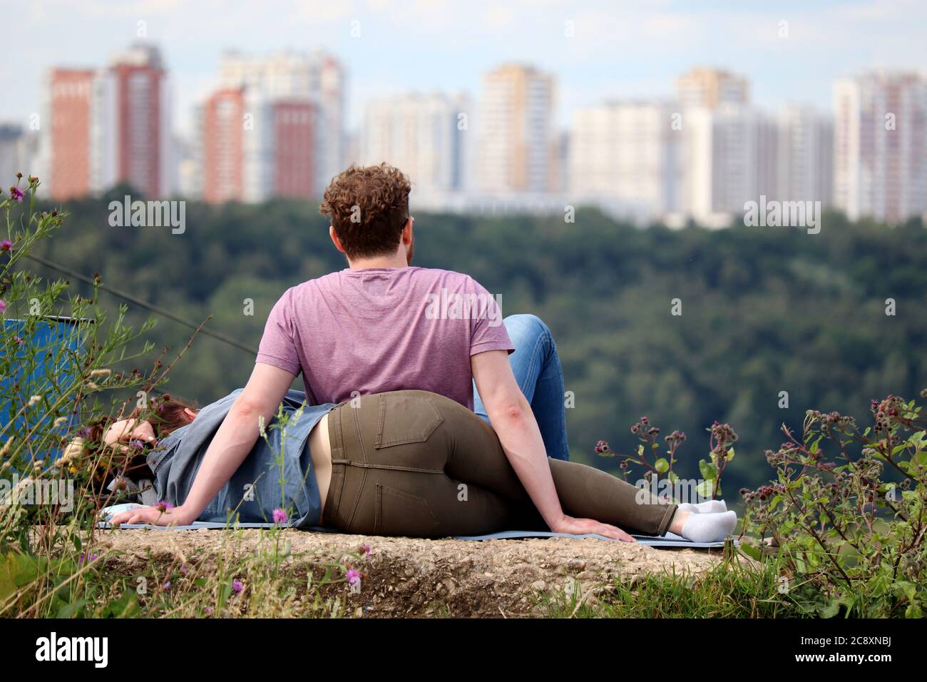 Verliebtes Paar, das auf einem Hügel auf einem Stadthintergrund sitzt. Sommer Freizeit und Entspannung, romantische Datum in einem Park Stockfoto