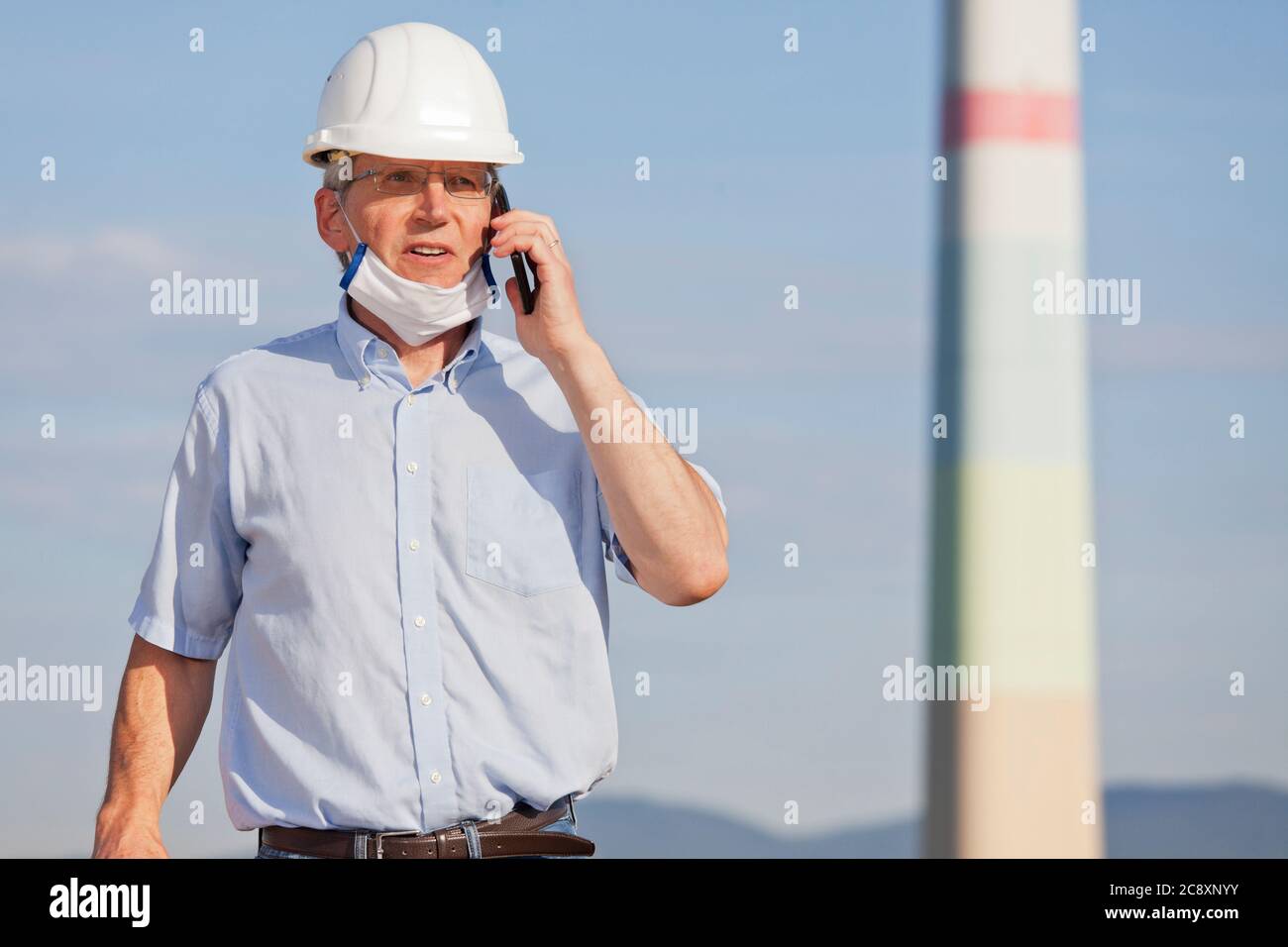 Leitender oder reifer Ingenieur, Architekt oder Inspektor mit Gesichtsmaske beim Telefonieren auf einer Baustelle oder Fabrik - selektiver Fokus Stockfoto