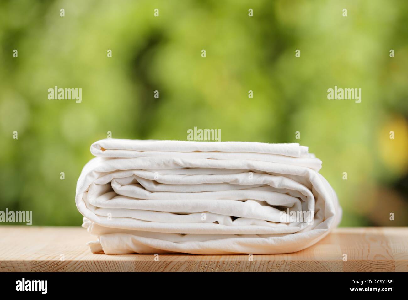 Ein Stapel gefaltetes weißes Bettzeug. Bettlaken auf unscharfem Blatthintergrund. Stockfoto