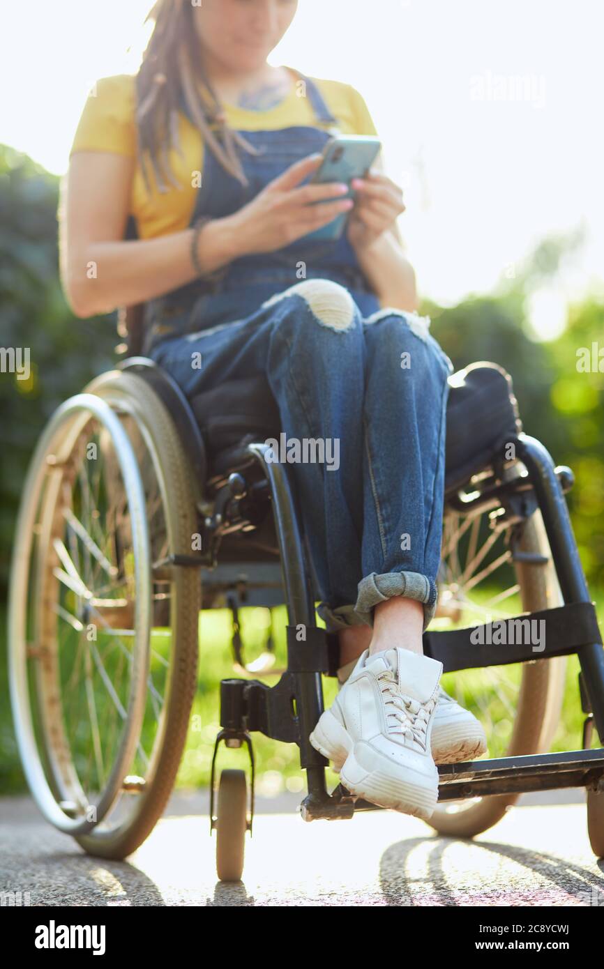 Junge attraktive Frau im Rollstuhl SMS mit ihrem Handy, Behinderung und Beschäftigungskonzept. Nahaufnahme abgeschnitten Foto. Verschwommener Hintergrund. fre Stockfoto