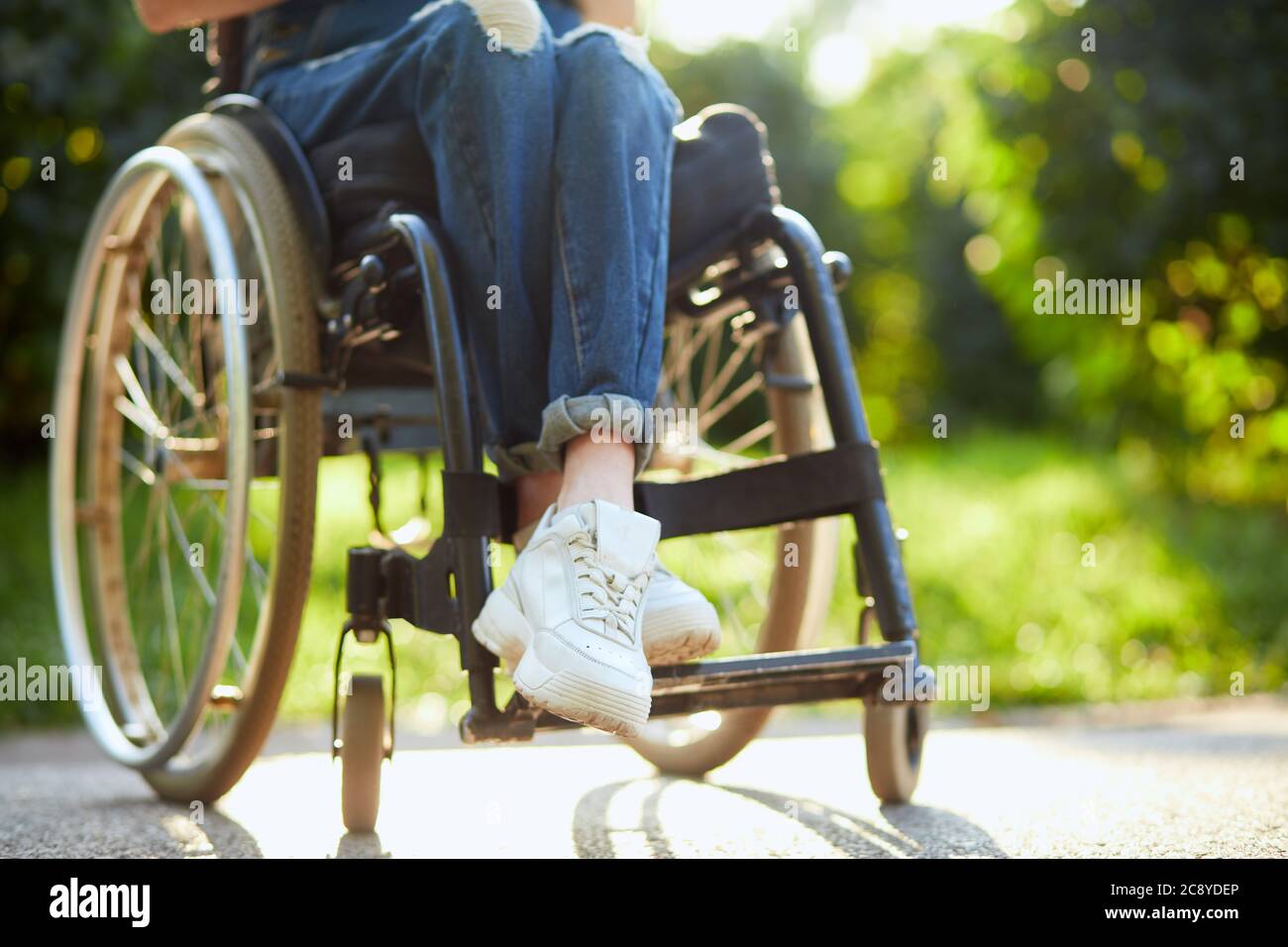 Junge behinderte Mädchen in insgesamt und weißen Turnschuhen sitzen mit gekreuzten Beinen auf dem Rollstuhl. Nahaufnahme abgeschnitten Foto. Stockfoto