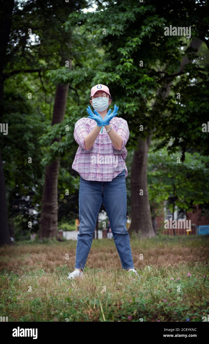 Eine asiatisch-amerikanische Frau, wahrscheinlich Chinesen, nimmt an einem Tai Chi Kurs im Freien Teil, während sie eine chirurgische Maske und Gummihandschuhe trägt. In Flushing, Queens, NYC Stockfoto