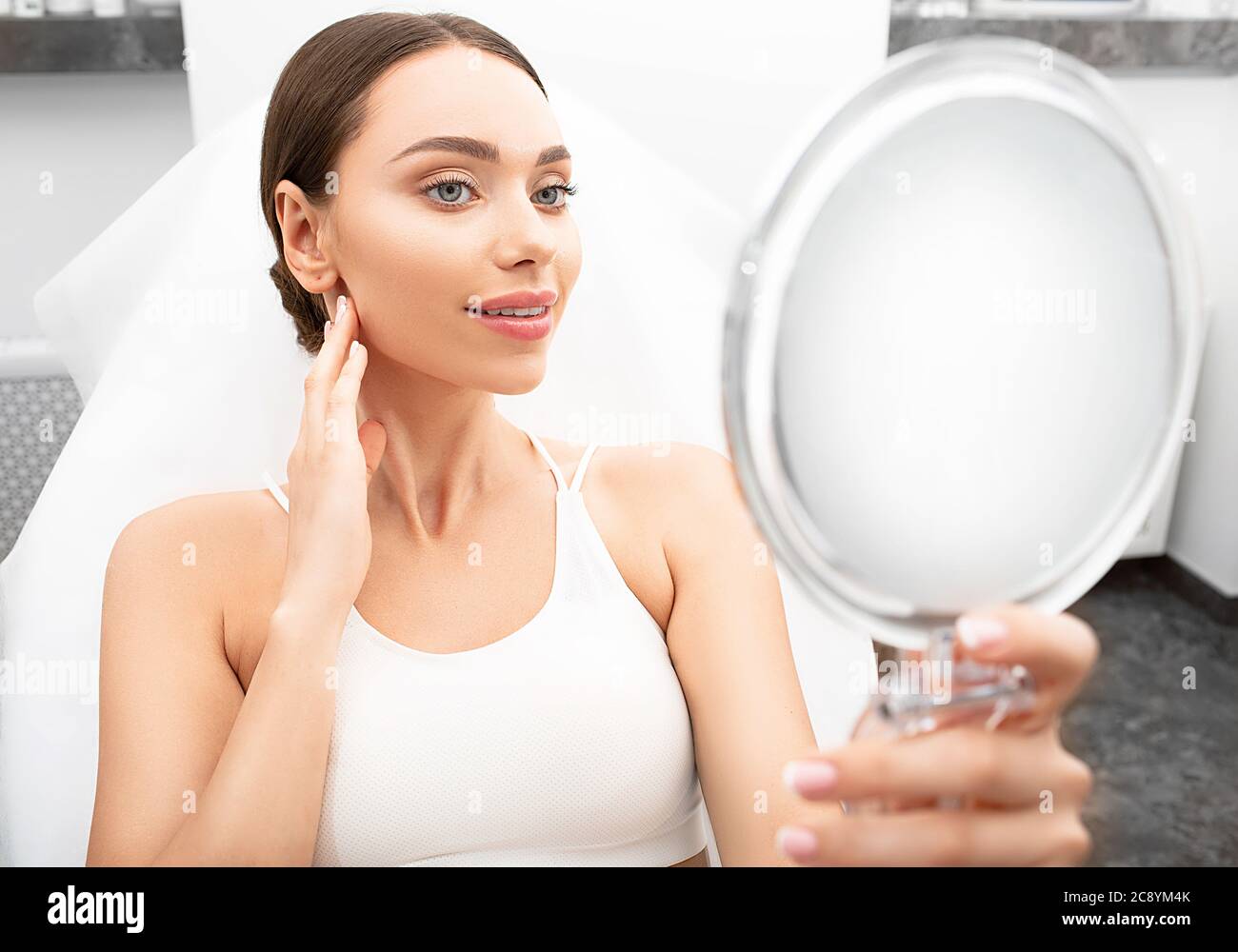 Eine schöne Frau mit einer frischen Gesichtshaut sieht im Spiegel, während sie im Büro der Kosmetikerin sitzt. Kosmetik und Hautbehandlung, schöne Gesundheit Stockfoto