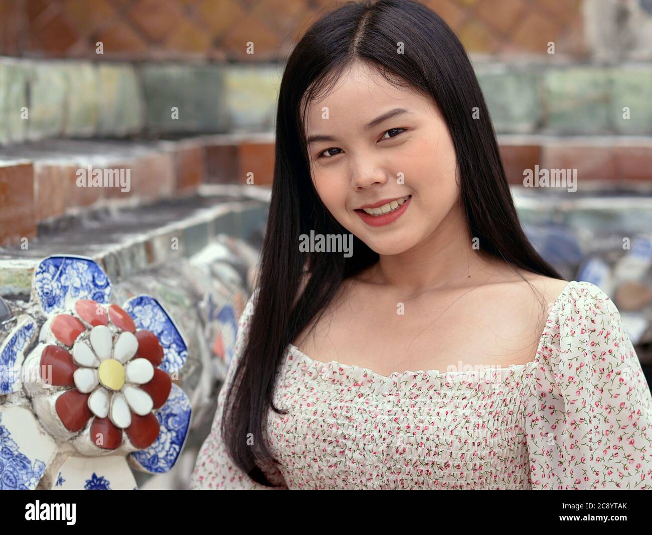 Hübsches Thai-Mädchen mit langen Haaren lächelt für die Kamera in Bangkoks berühmtem Wat Arun Tempel. Stockfoto