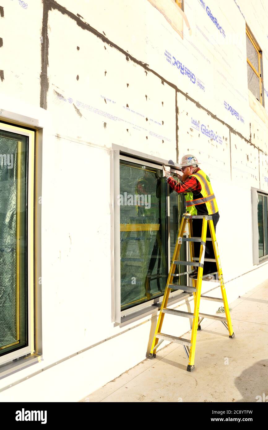 Ein Glasurglas auf einer Leiter, das Wetterdichtmittel um die Kanten der neu installierten Fenster auf einer Baustelle aufgibt. Stockfoto
