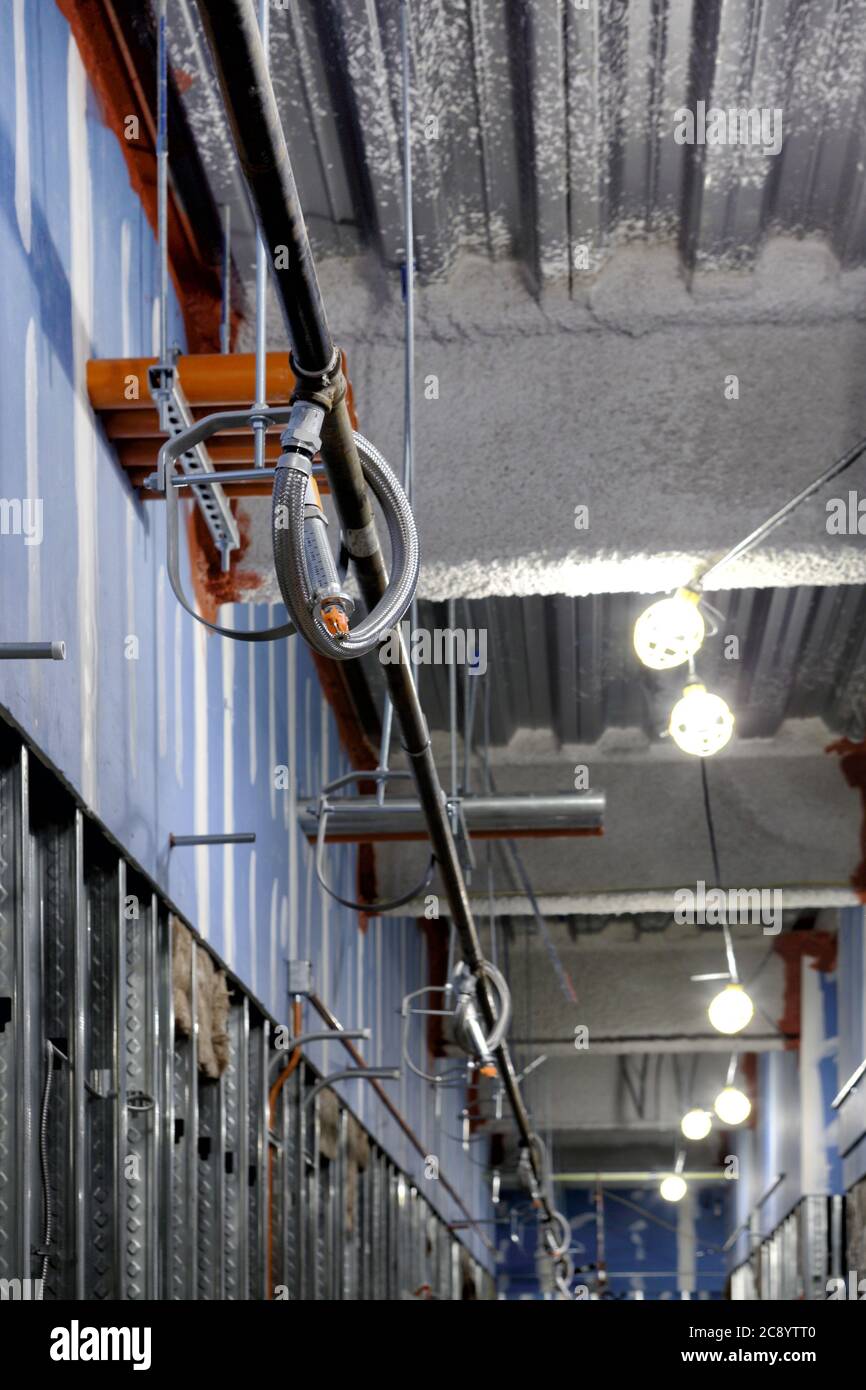 Ein Innenkorridor eines Gebäudes im Bau, mit provisorischen Arbeitsleuchten, freiliegenden Stehbolzen, Feuerlöschanlage und elektrischen Leitungen. Stockfoto