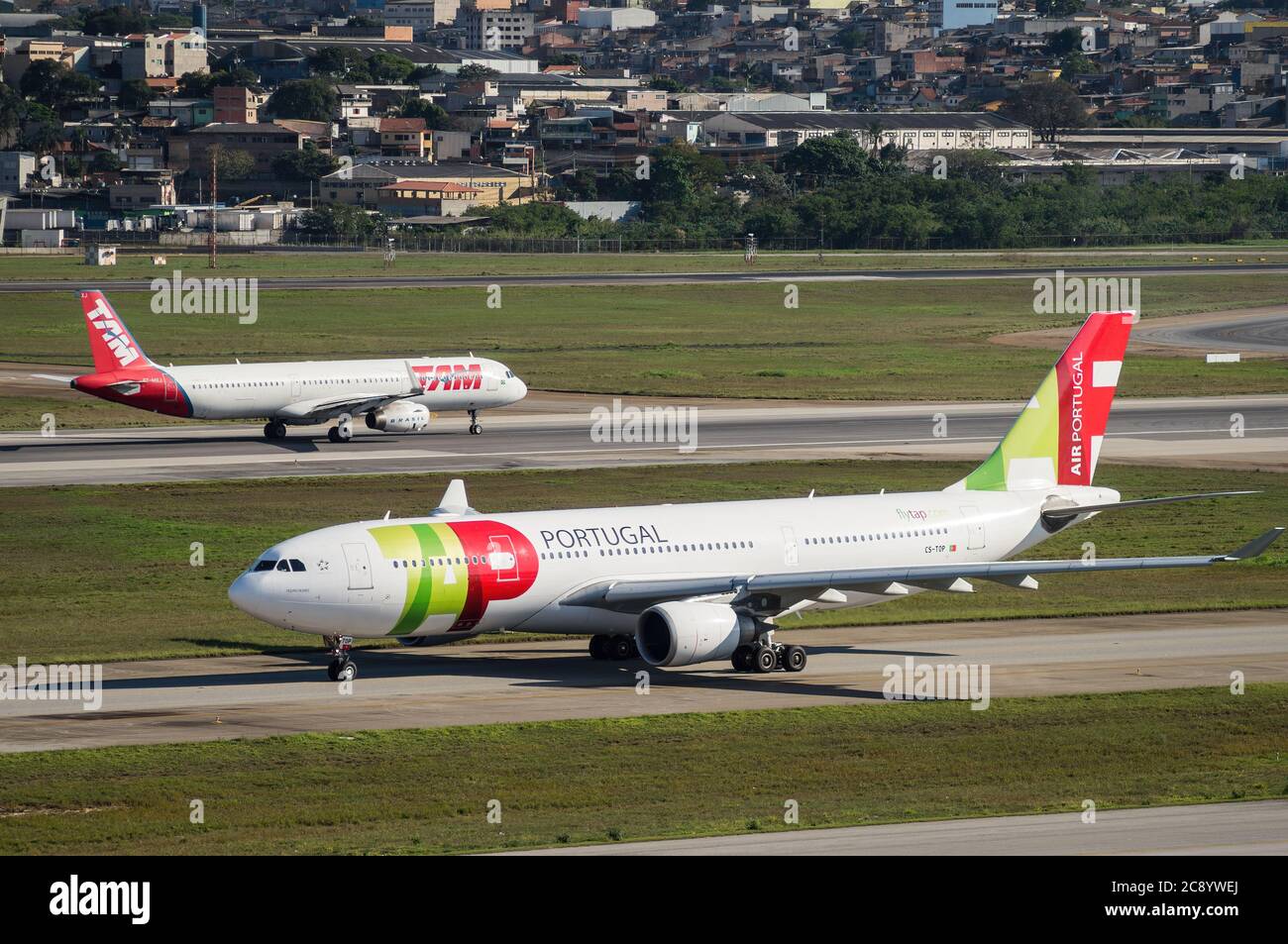 TAP Air Portugal Airbus A330-202 (CS-TOP - 'Pedro Nunes') besteuert, während ein weiteres Flugzeug auf der Piste 27R von Sao Paulo/Guarulhos Intl abfliegt. Flughafen. Stockfoto