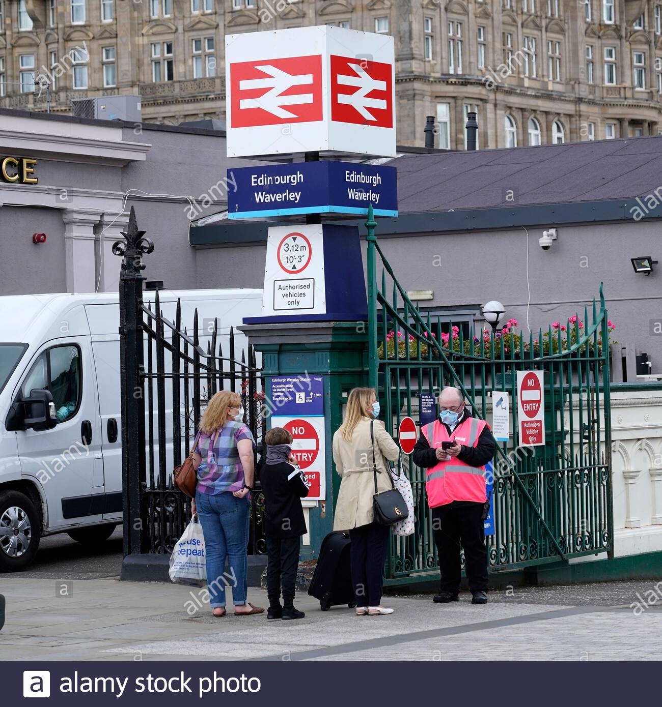 Menschen, die Gesichtsmasken tragen und mit einem Scotrail-Mitarbeiter in einer Hi-viz-Jacke vor der Waverley Station in Edinburgh sprechen Stockfoto