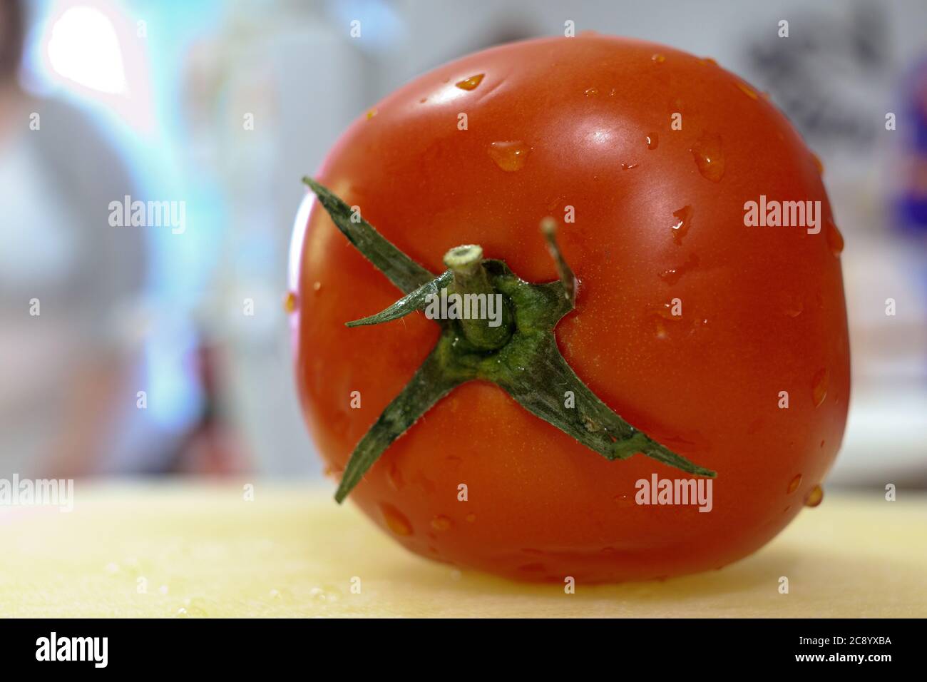 Eine frische, gewaschene rote Tomate mit grünem Stiel sitzt auf einem Schneidebrett mit Wassertropfen darauf. Stockfoto