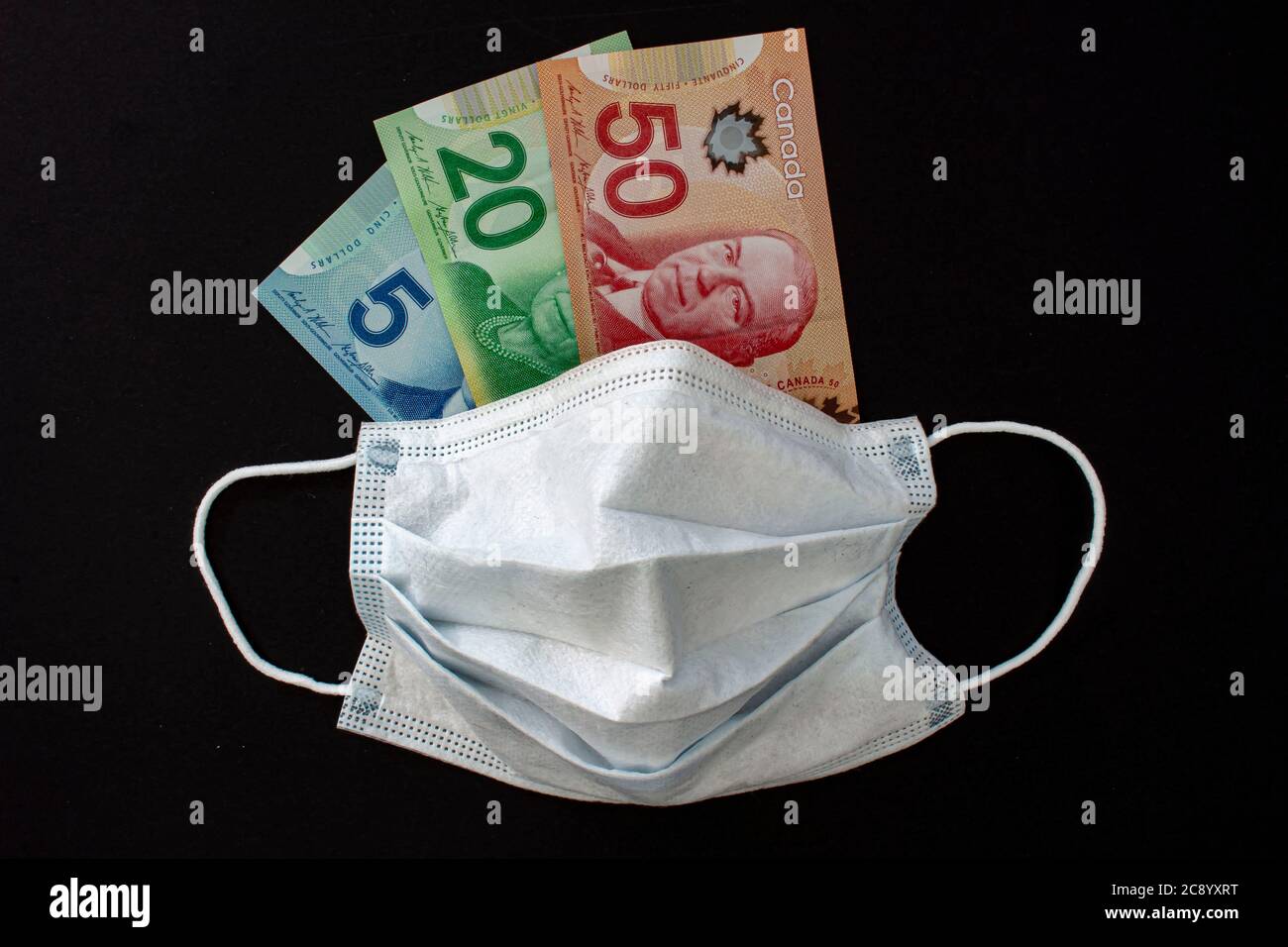 Calgary, Alberta, Kanada. Juli 26, 2020. Eine Gesichtsmaske mit kanadischen Dollar-Scheinen auf schwarzem Hintergrund. Stockfoto