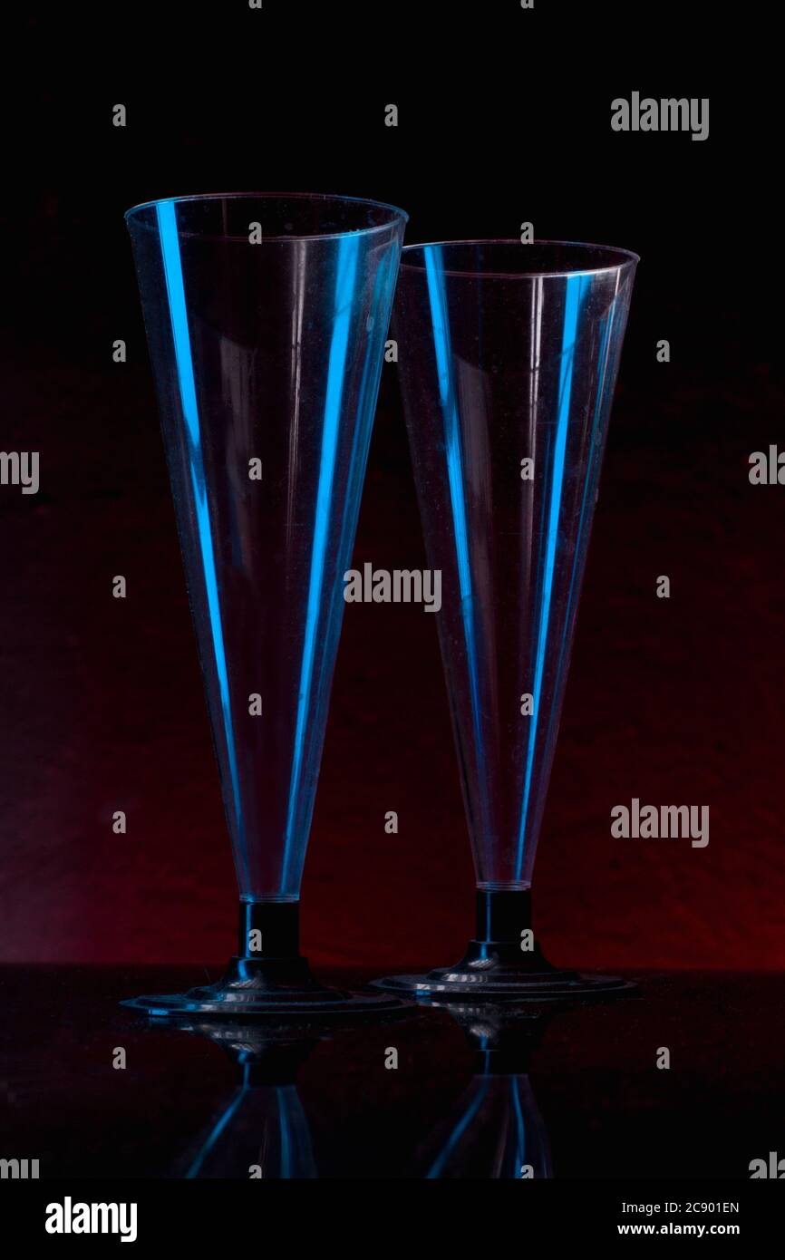 Zwei transparente blaue Gläser, die in dezenter Beleuchtung über dem roten dunklen Hintergrund isoliert aufgenommen wurden. Stockfoto