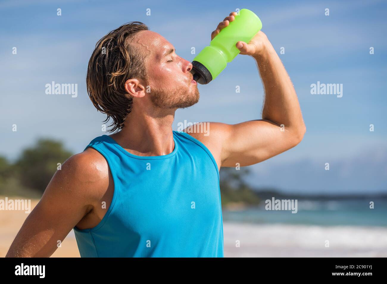 Sport Flasche trinken Sport Mann Trinkwasser am Strand laufen. Männlicher Läufer verschwitzt und durstig nach schwierigem Training Stockfoto