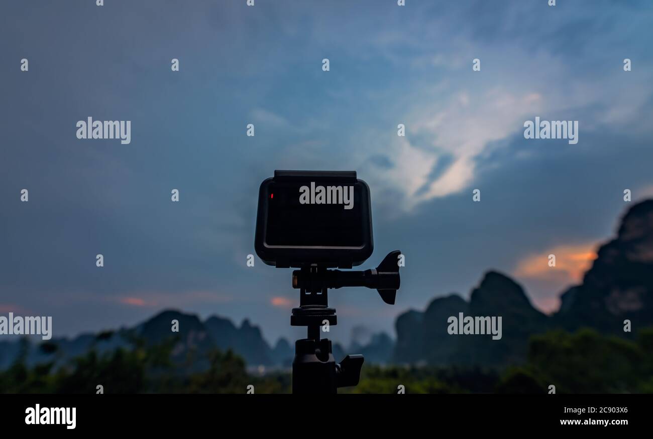 Kleine tragbare Action-Kamera auf einem Stativ, die Zeitraffer-Videos von einem Sonnenuntergang über der wunderschönen beeindruckenden Karstgebirgslandschaft in Yangshuo, Guangx, aufzeichnet Stockfoto