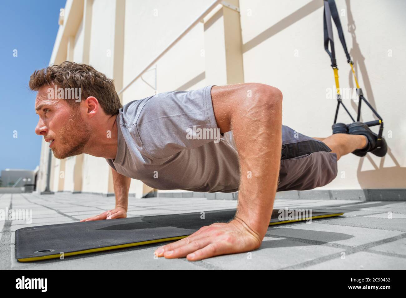Fitness-Mann tut Liegestütze mit Aufhängebänder im Fitnesscenter. Sportler, der im Freien Übungen zum Liegestütze auf dem Boden macht Stockfoto