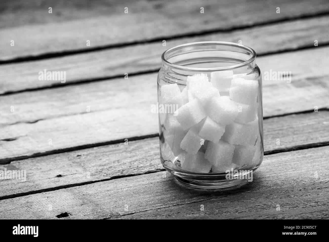 Der raffinierte Zucker in den Würfeln im Glas die Kapazität auf dem hölzernen Hintergrund aus den alten Brettern, niemand. Stockfoto