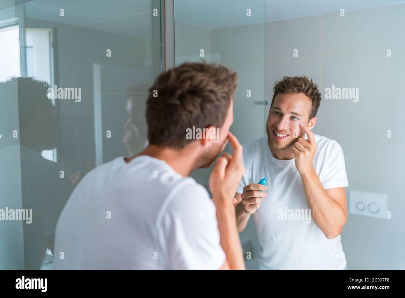 Glücklicher junger Mann kümmert sich um seine Unterauge Falten Putting Anti-Aging-Augencreme Stockfoto