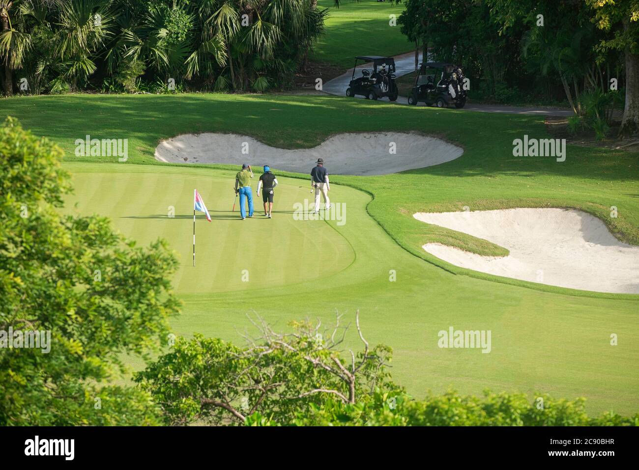 Eine Gruppe von Freunden auf dem Golfplatz, die eine gute Zeit haben. Sie gehen Seite an Seite in einem spielerischen Gespräch mit ihren Golfwagen - Playa del Carmen, Mexiko Stockfoto