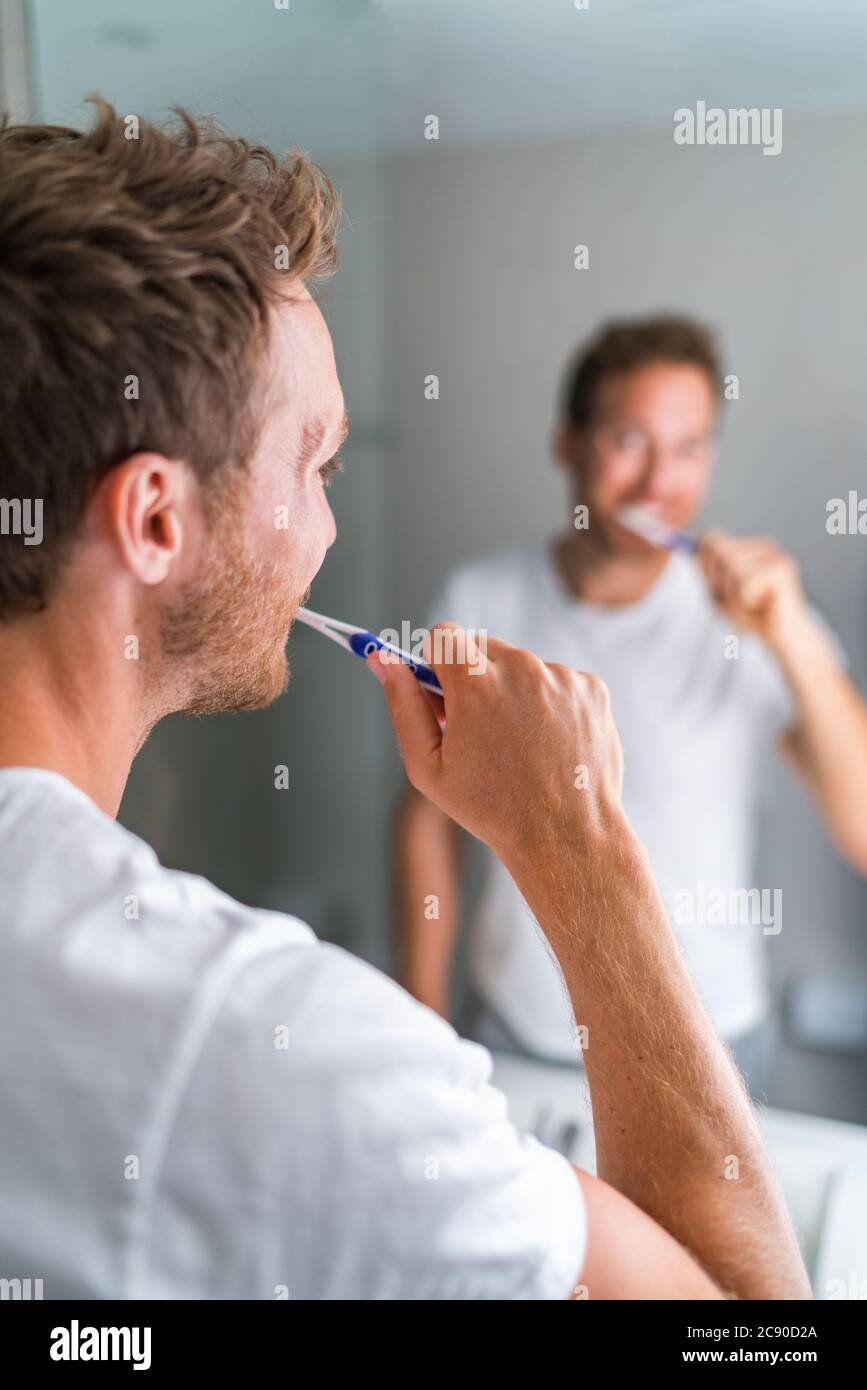 Der Mann, der morgens die Zähne putzte, schaute im Badezimmerspiegel mit Zahnbürste und Zahnpasta. Home Lifestyle, Zahnhygiene Pflege. Mundgesundheit Stockfoto