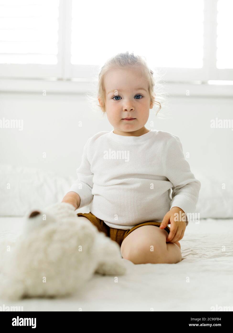 Lächelndes Kleinkind Mädchen sitzt auf dem Bett mit Teddybär Spielzeug Stockfoto