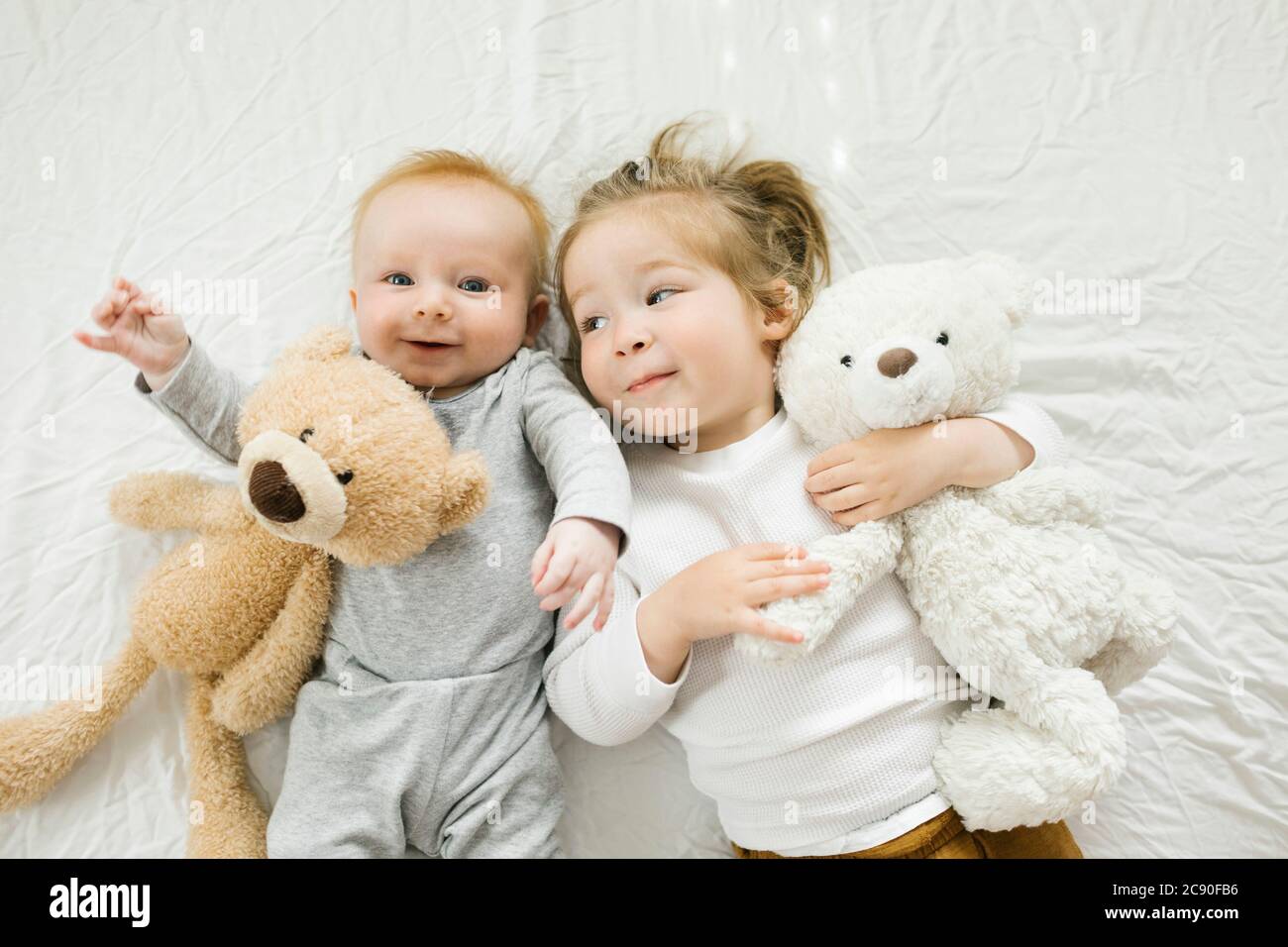 Porträt von Geschwistern, die mit ihren Teddybären auf dem Bett liegen Stockfoto