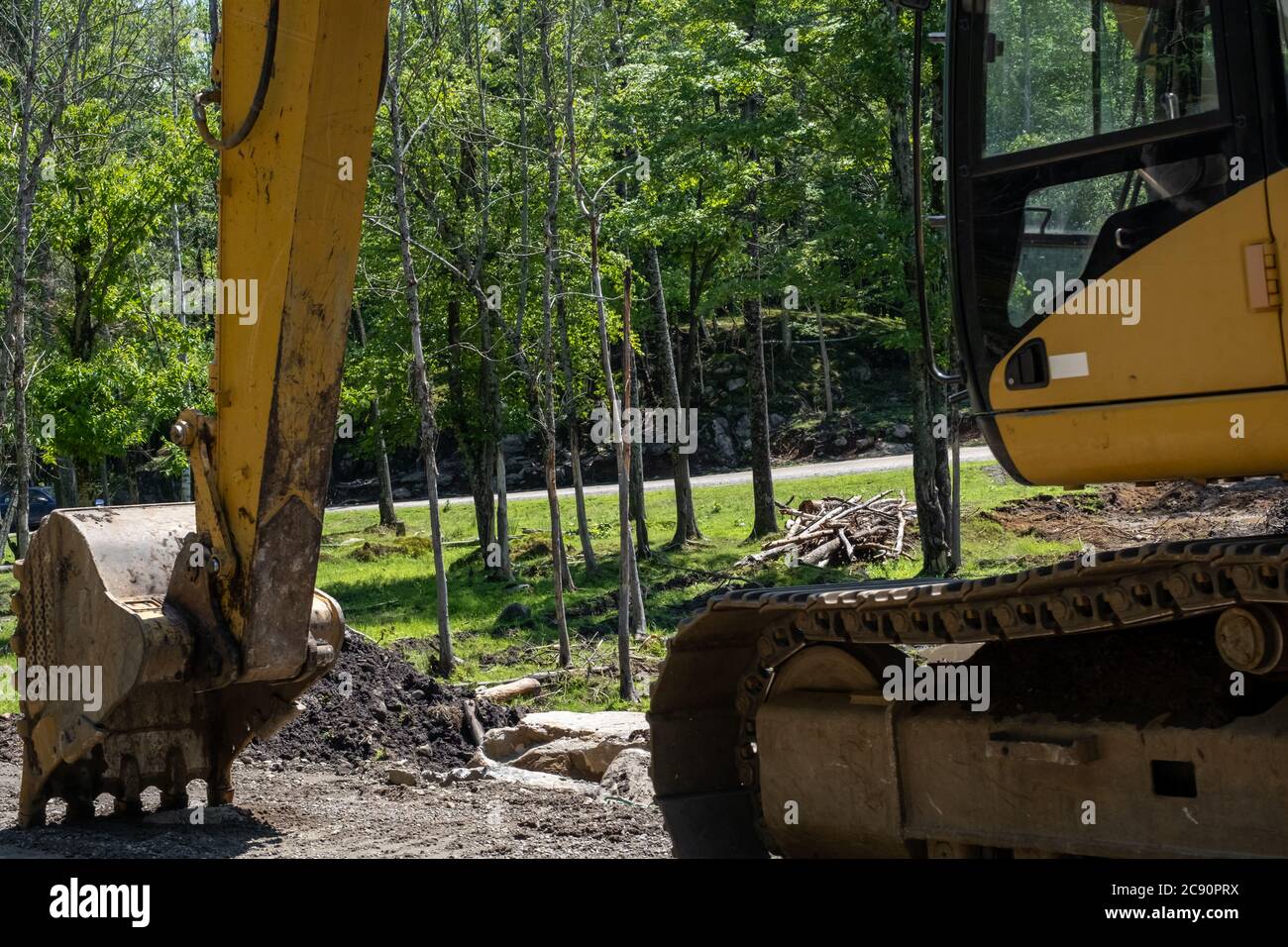 An der Seite einer unbefestigten Fahrbahn ist ein Bagger geparkt. Aus der Nähe betrachtet zeigt seine Metallschaufel, die in den Kies drückt, die gelbe Konstruktion Stockfoto