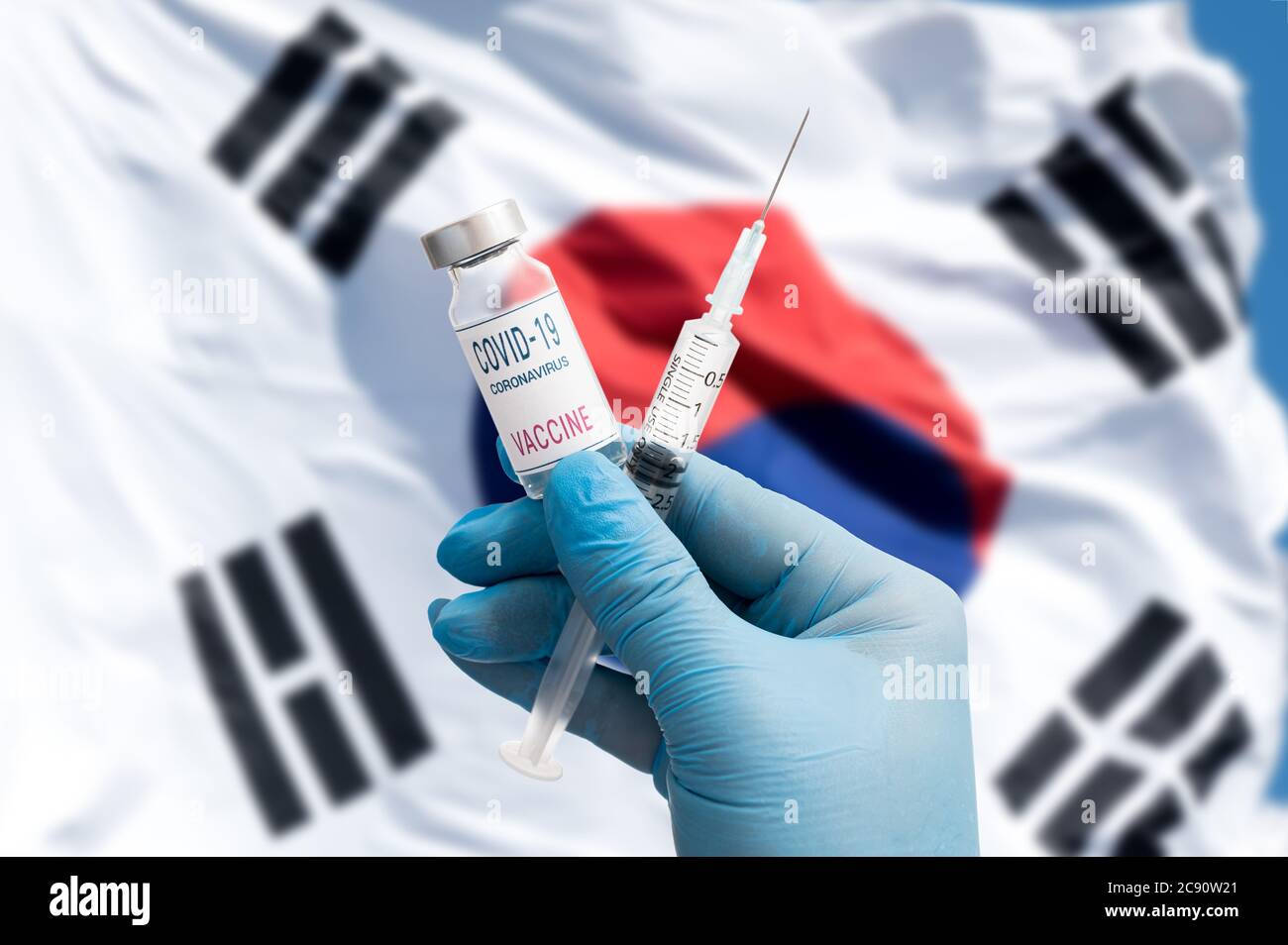 Die Hände eines Arztes, der den Cobid-19-Impfstoff mit blauen Handschuhen vor dem Hintergrund des Taegeukgi hält. Stockfoto