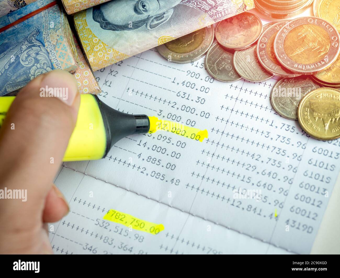 Nahaufnahme Hand mit gelben Marker Stift Hervorhebung auf dem Einzahlungsgeld, Kontoauszug in Sparkonto Passbook mit Geld, Banknote und Münzen. Stockfoto