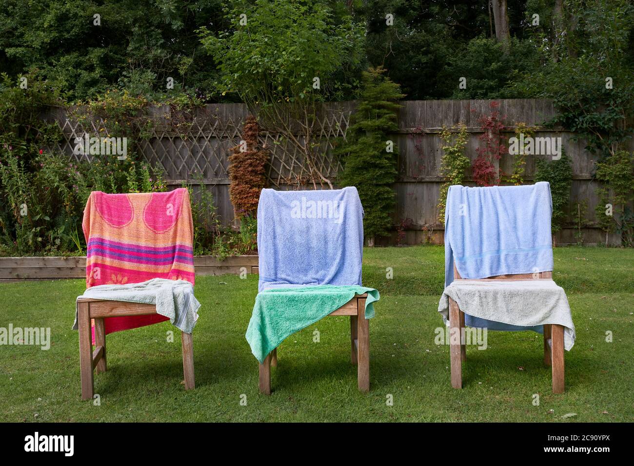 Nasse Handtücher drapiert über Holzstühlen in einem Garten in einem sonnigen Moment nach einem Sturm trocknen. Stockfoto