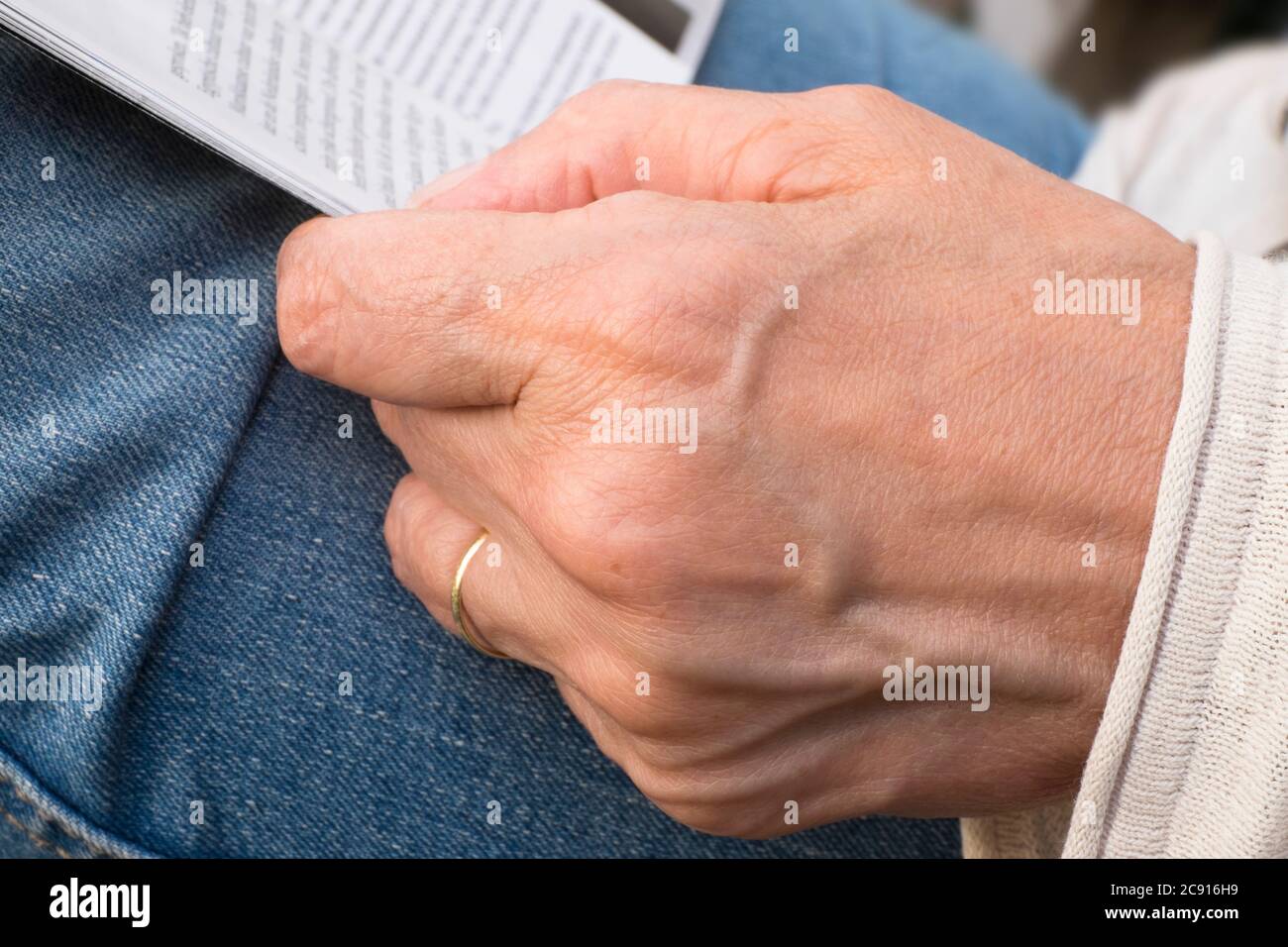 Nahaufnahme der Hände einer Frau beim Lesen eines Papiers oder einer Zeitschrift, geringe Schärfentiefe. Die Hand ruht auf Jeans Stockfoto