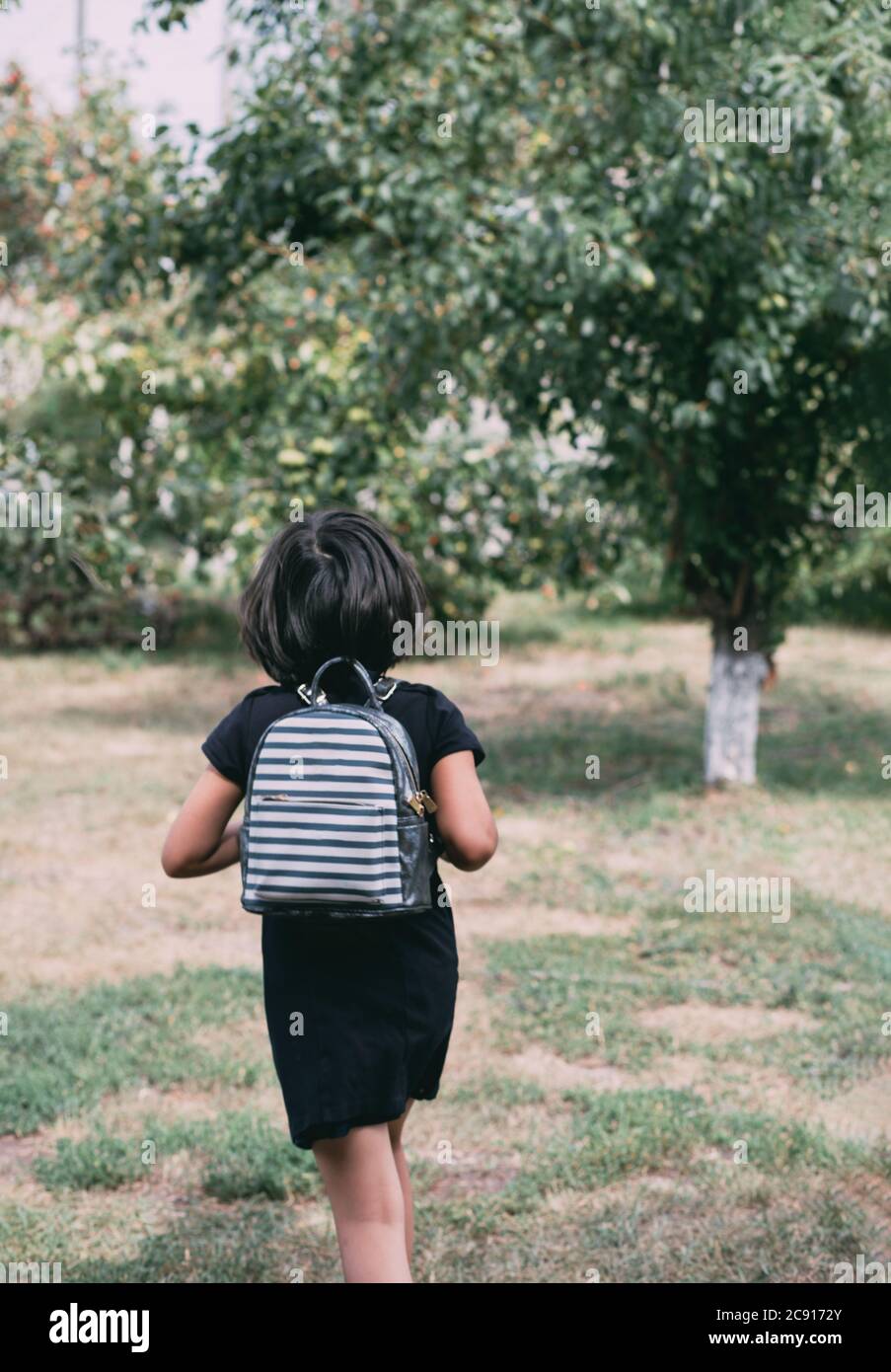 Zurück zur Schule. Kleines Mädchen mit Rucksack läuft durch die Gasse. Kind aus der Grundschule. Stockfoto