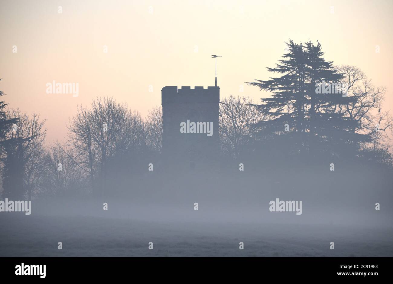 Nebel liegt auf einer frostigen Wiese vor einer Kirche auf diesem Foto, das an einem kalten Morgen im Dezember aufgenommen wurde Stockfoto