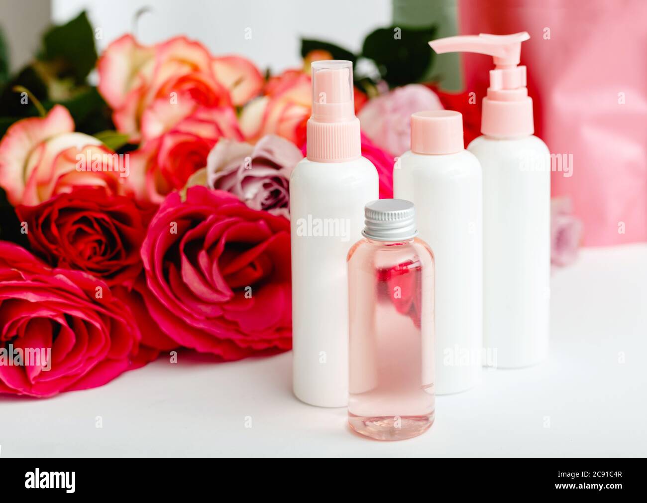 Kunststoff-Kosmetikflaschen, Serum, Seife, Öl auf weißem Tisch floralen Hintergrund. Blume rot rosa Rosen natürliche organische Schönheit Produkt. Spa, Hautpflege Stockfoto