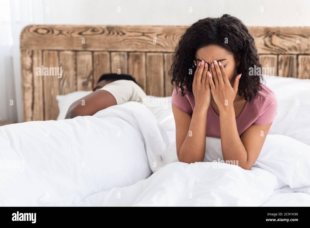 Weinende afrikanische Frau sitzt auf dem Bett neben schlafenden Mann Stockfoto
