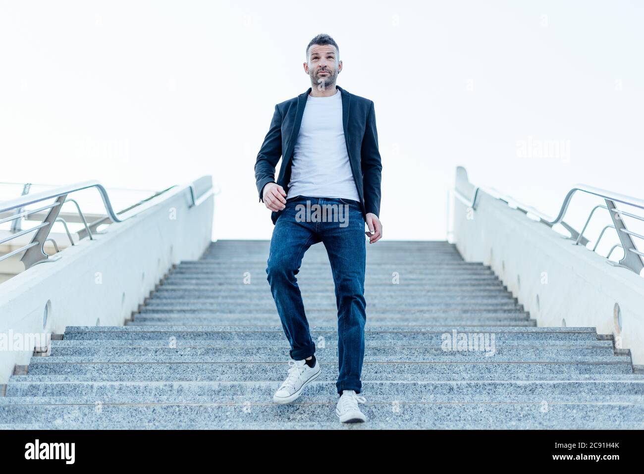 Lässige stilvolle junge Mann in Jacke und Jeans zu Fuß die Treppe hinunter, im Freien Stockfoto