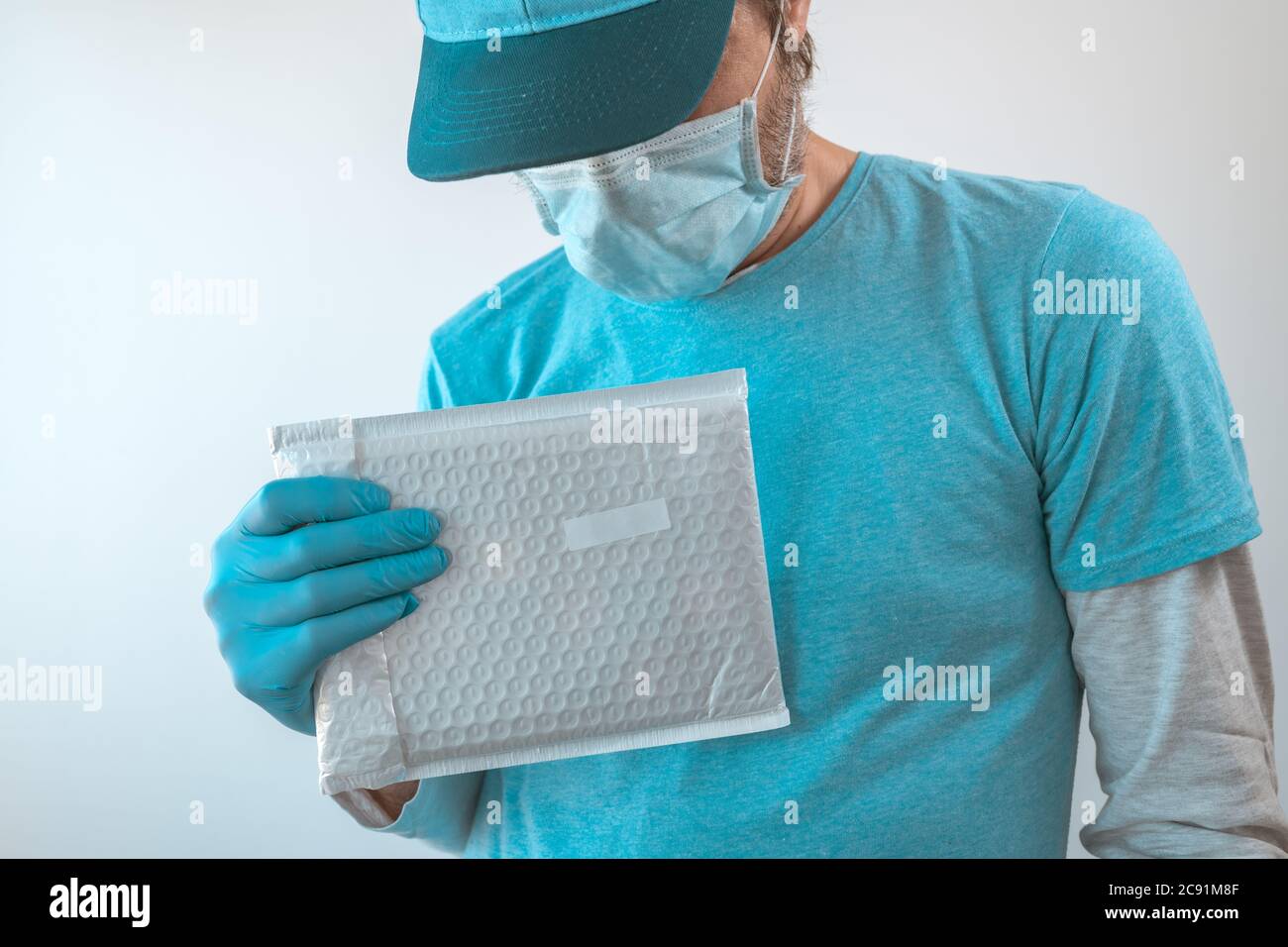 Lieferung Mann posiert mit Paket in Schutzkleidung tragen Baseball-Kappe, Schutzmaske und Handschuhe während Virusinfektion Pandemie outbre Stockfoto