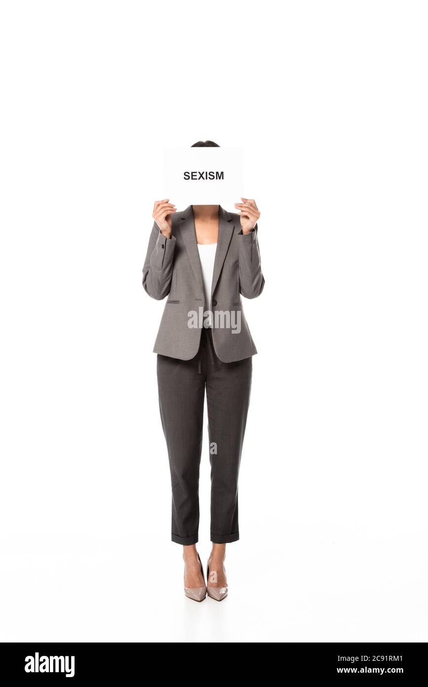 Geschäftsfrau im Anzug, das Gesicht bedeckt, während sie Plakat mit Sexismus-Schriftzug auf Weiß isoliert hält Stockfoto