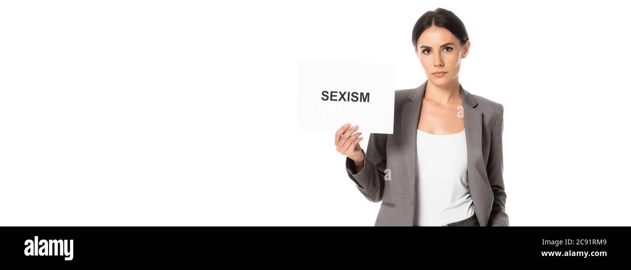 Panoramischer Ausschnitt von attraktiven Geschäftsfrau hält Plakat mit Sexismus Schriftzug isoliert auf weiß Stockfoto