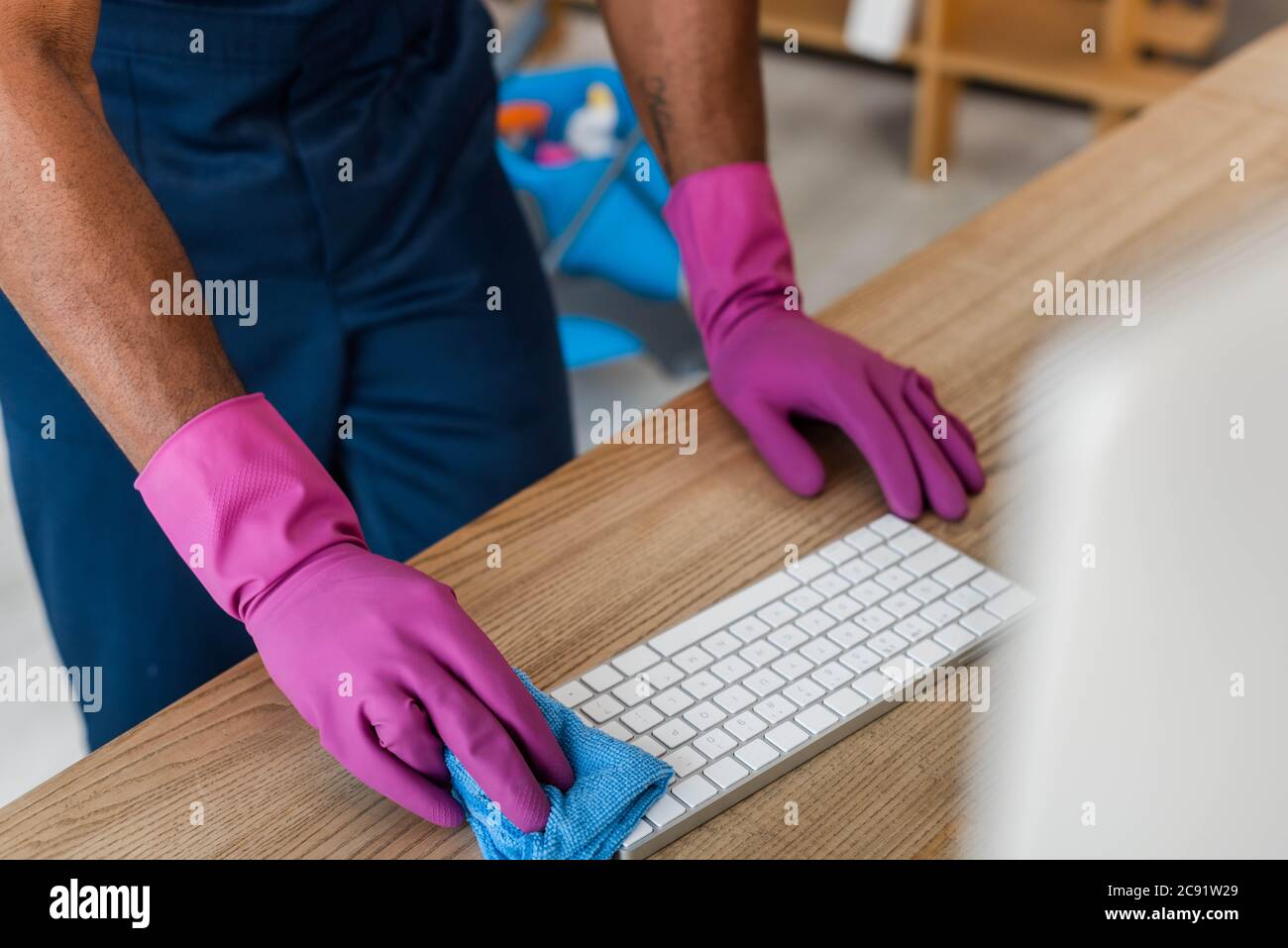 Beschnittene Ansicht der afroamerikanischen Reiniger in Gummihandschuhen Reinigung Computer-Tastatur im Büro Stockfoto