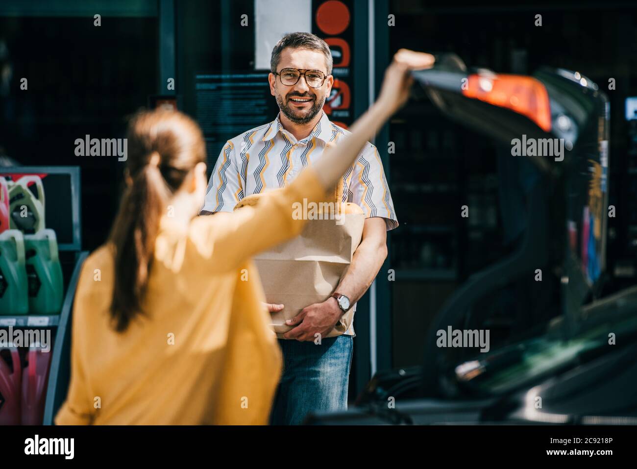 Selektiver Fokus auf lächelnden Mann, der Einkaufstasche hält und Frau in der Nähe des Autos auf der städtischen Straße anschaut Stockfoto