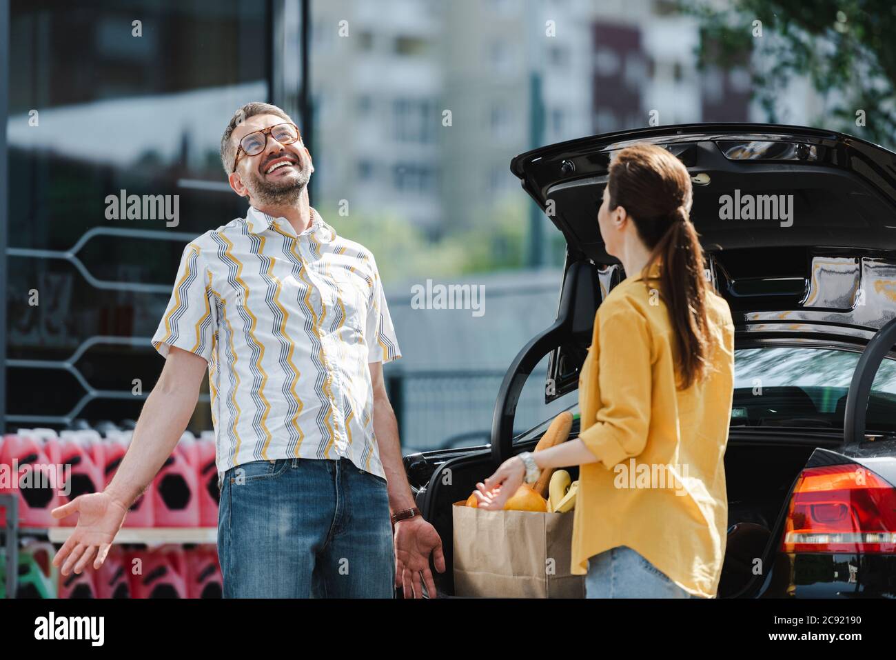 Selektiver Fokus von lächelnden Mann in der Nähe von Frau und offenen Kofferraum des Autos auf der städtischen Straße Stockfoto