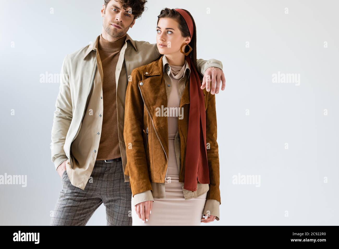 Schöner Mann hält Hand auf der Schulter der modischen Frau isoliert auf grau Stockfoto