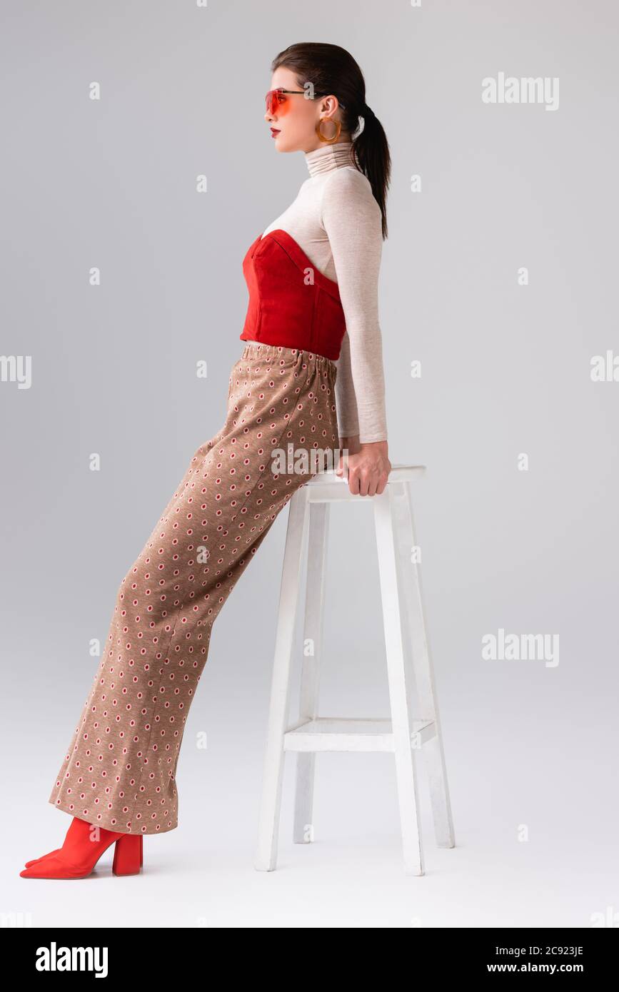 Seitenansicht der modischen Mädchen in beige Hose und roten Korsett auf  Rollkragen lehnt auf Hocker auf grau Stockfotografie - Alamy