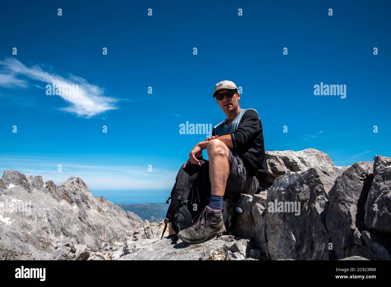 Ein Mann mittleren Alters sitzt auf der felsigen Bergspitze Stockfoto
