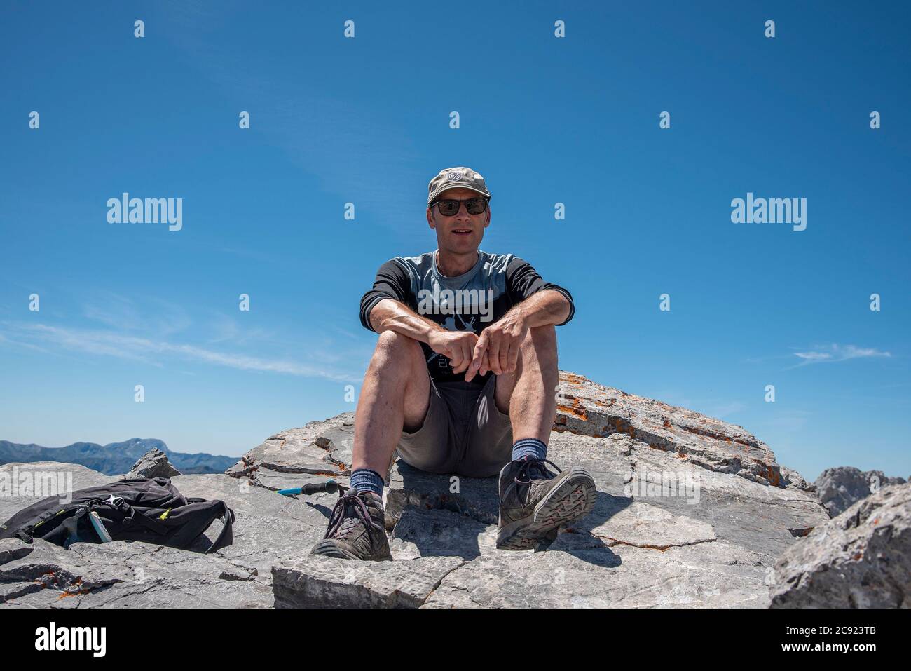 Ein Mann mittleren Alters sitzt auf der felsigen Bergspitze Stockfoto