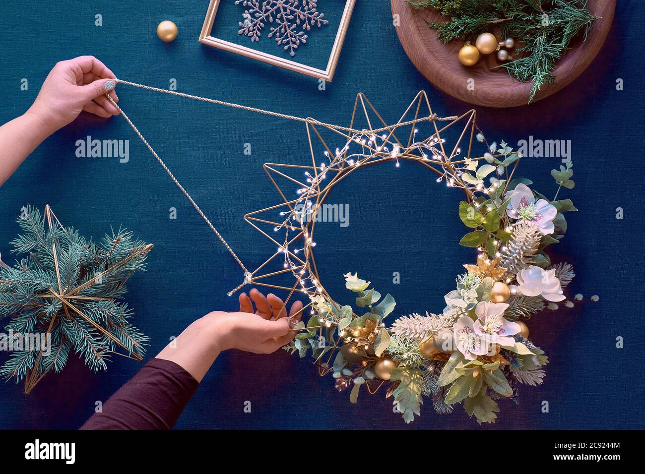 Weihnachtskranz machen, kreative flache legen, Draufsicht auf dunklem Hintergrund mit weiblichen Händen, handgefertigten Kranz, Weihnachtsdekorationen und Evergreens. Stockfoto