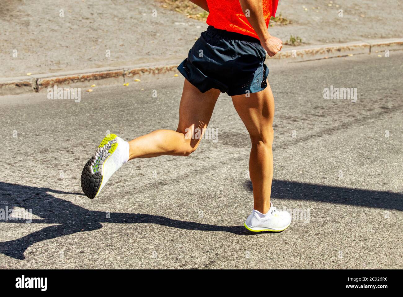 Männlicher Läufer läuft auf der Straße in hartem Licht. Schatten auf Asphalt Stockfoto