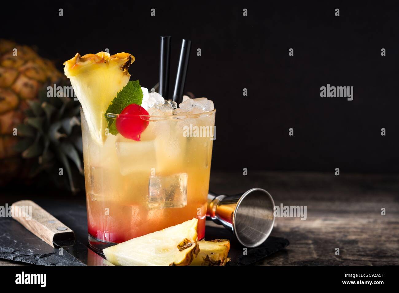 Kalter Mai Tai Cocktail mit Ananas und Kirsche im Glas auf schwarzem Hintergrund Stockfoto