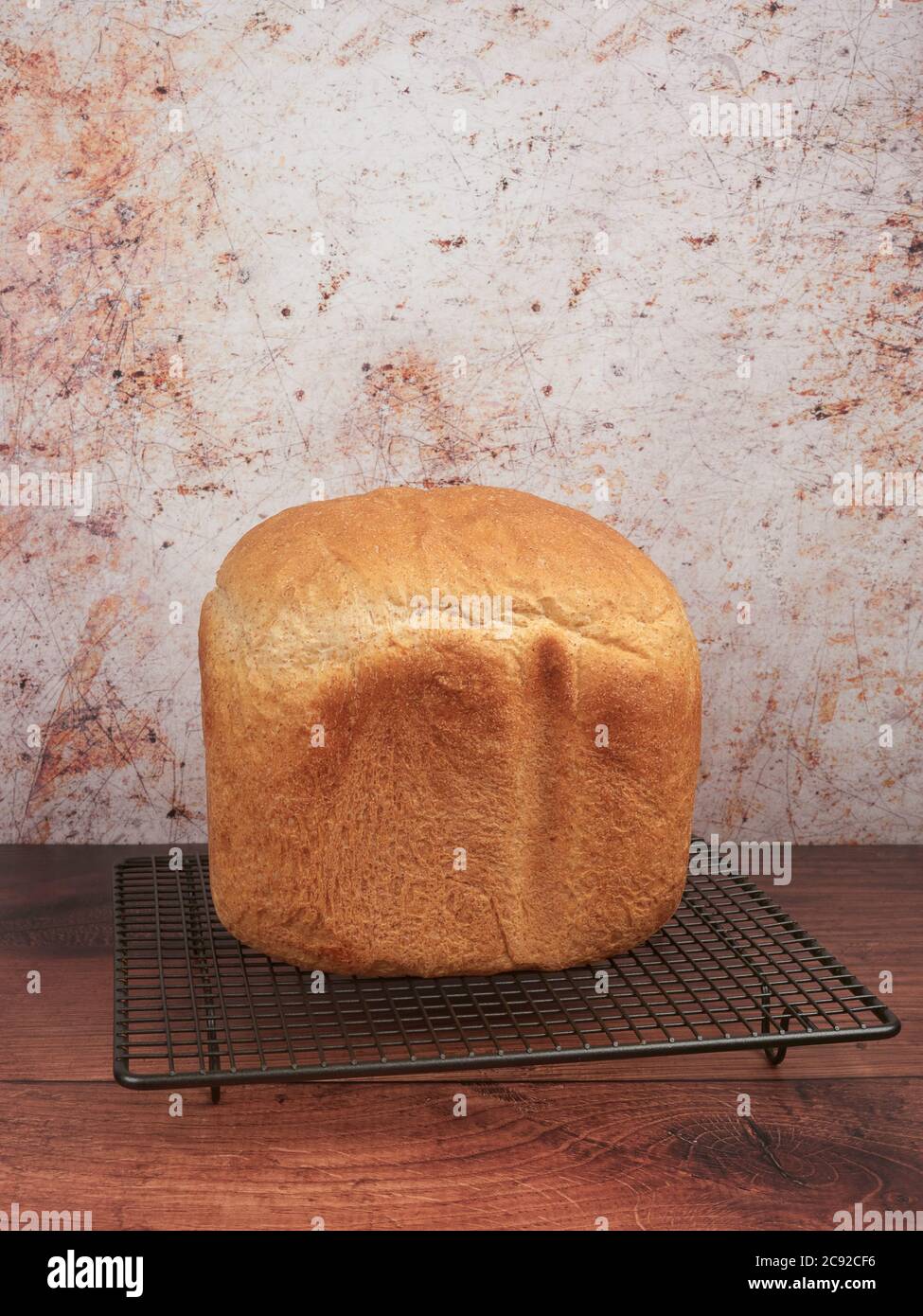 Frisches Brot zu Hause mit der Brotmaschine, auf einem grauen Kühlgestell, auf braunem Hintergrund Stockfoto